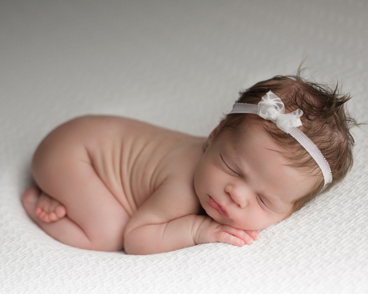 Новорожденная малышка с белой лентой на голове