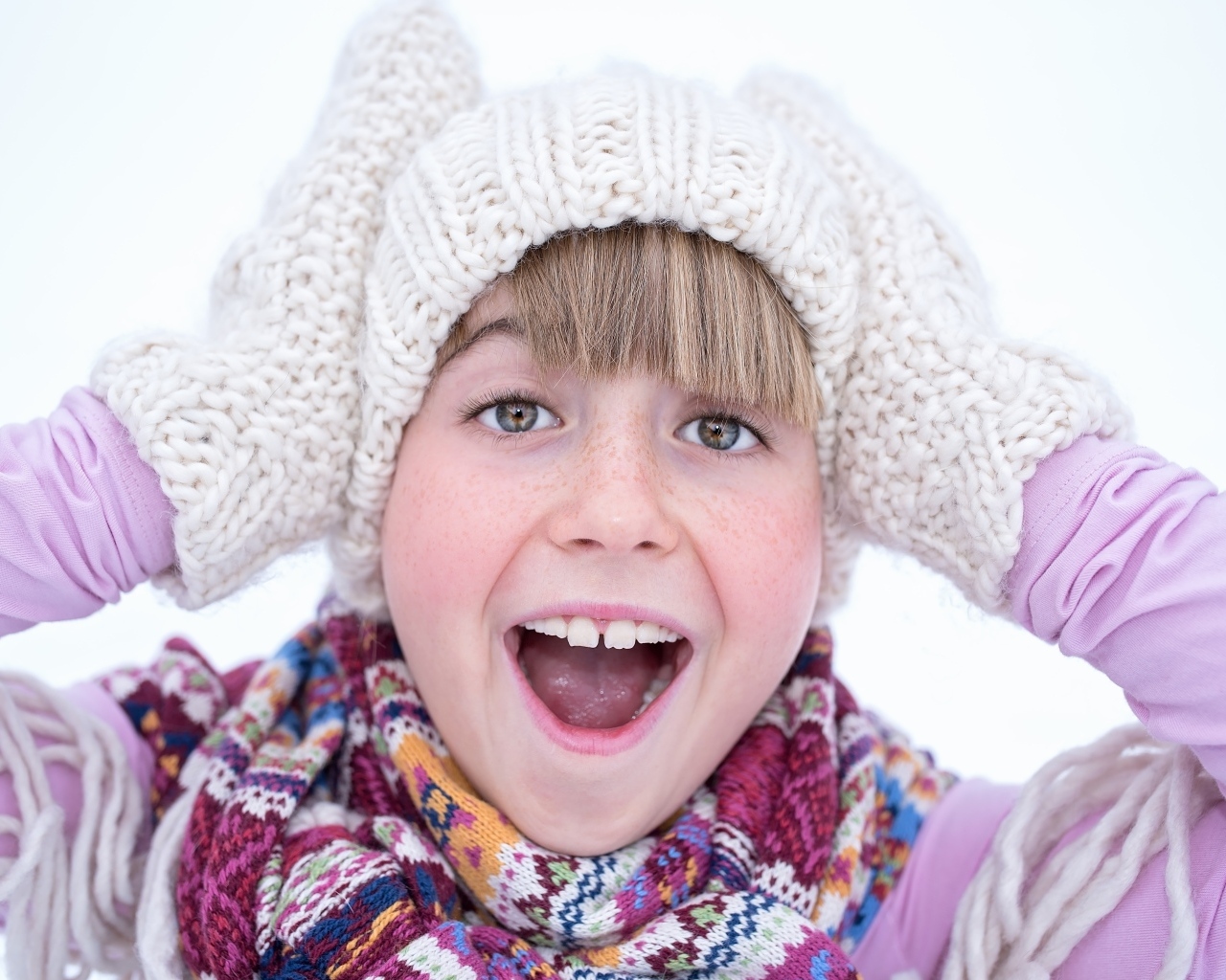 Довольная девочка в вязаной шапке и варежках