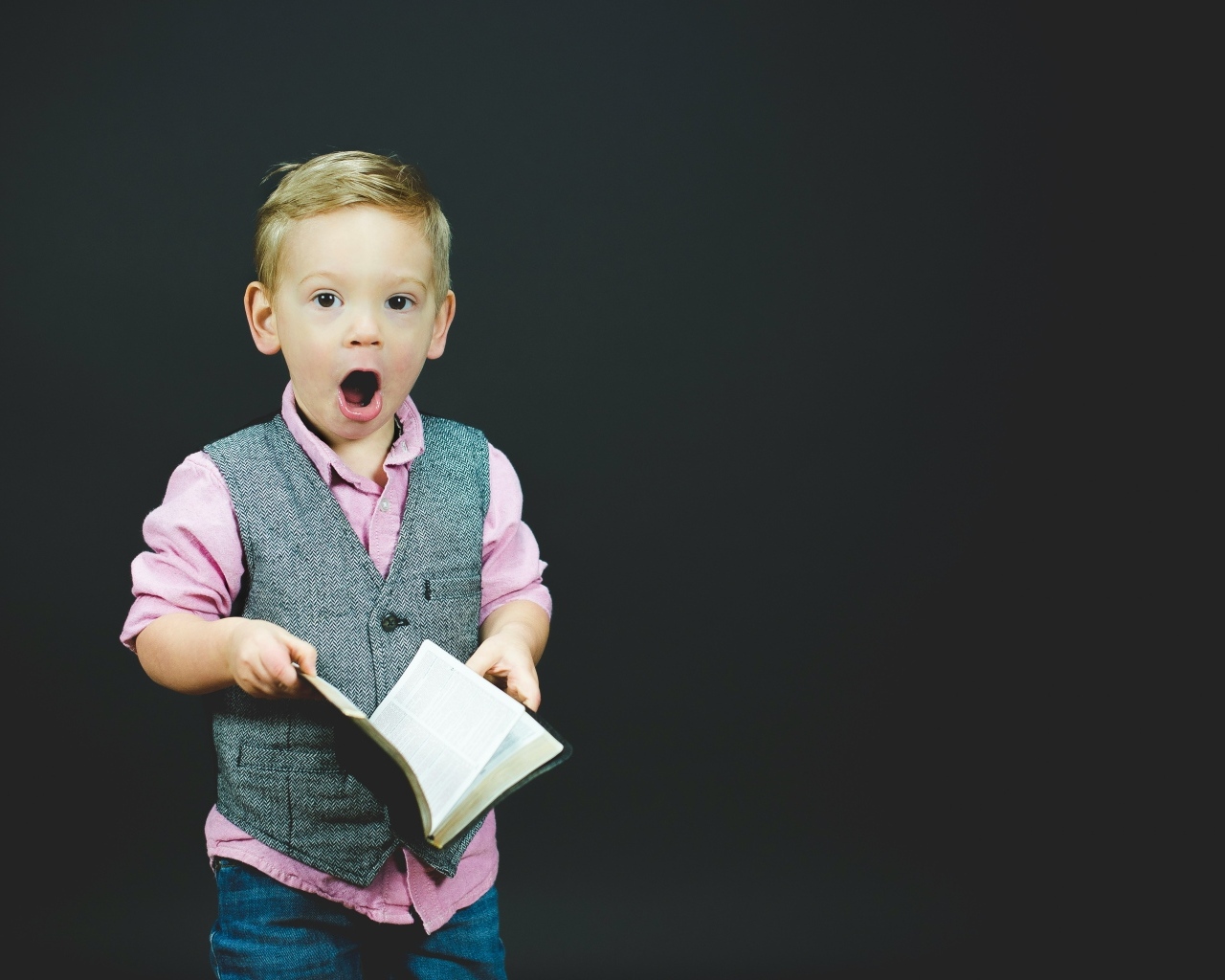 Удивленный мальчик с книгой в руках на черном фоне
