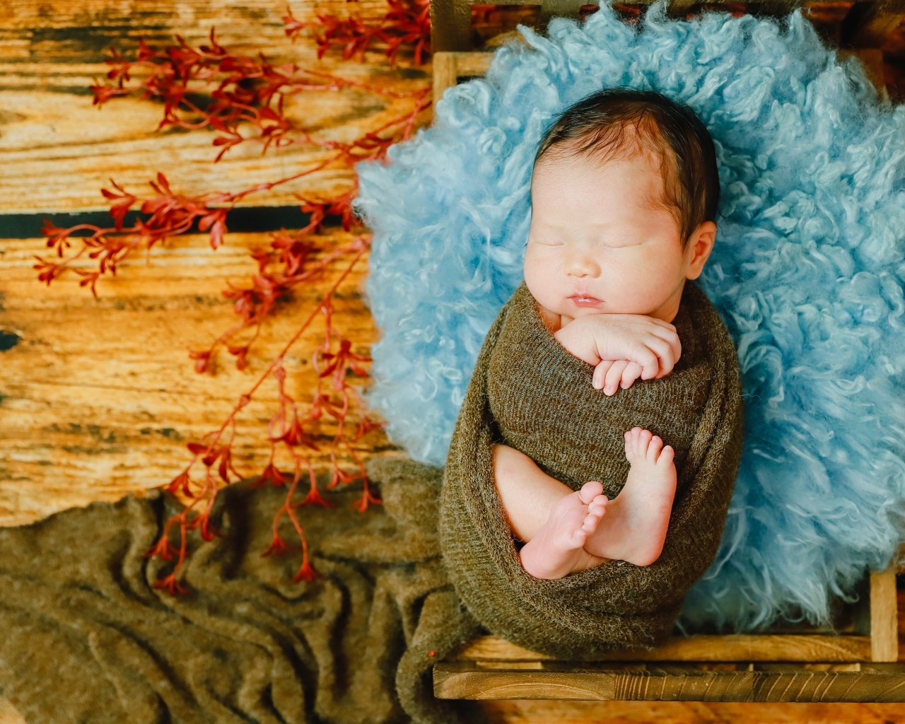 Крошечный новорожденный ребенок на голубой меховой подушке