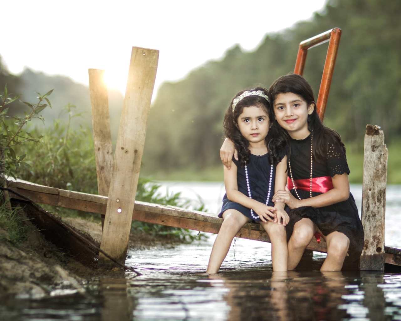 Две девочки сидят на мосту у реки