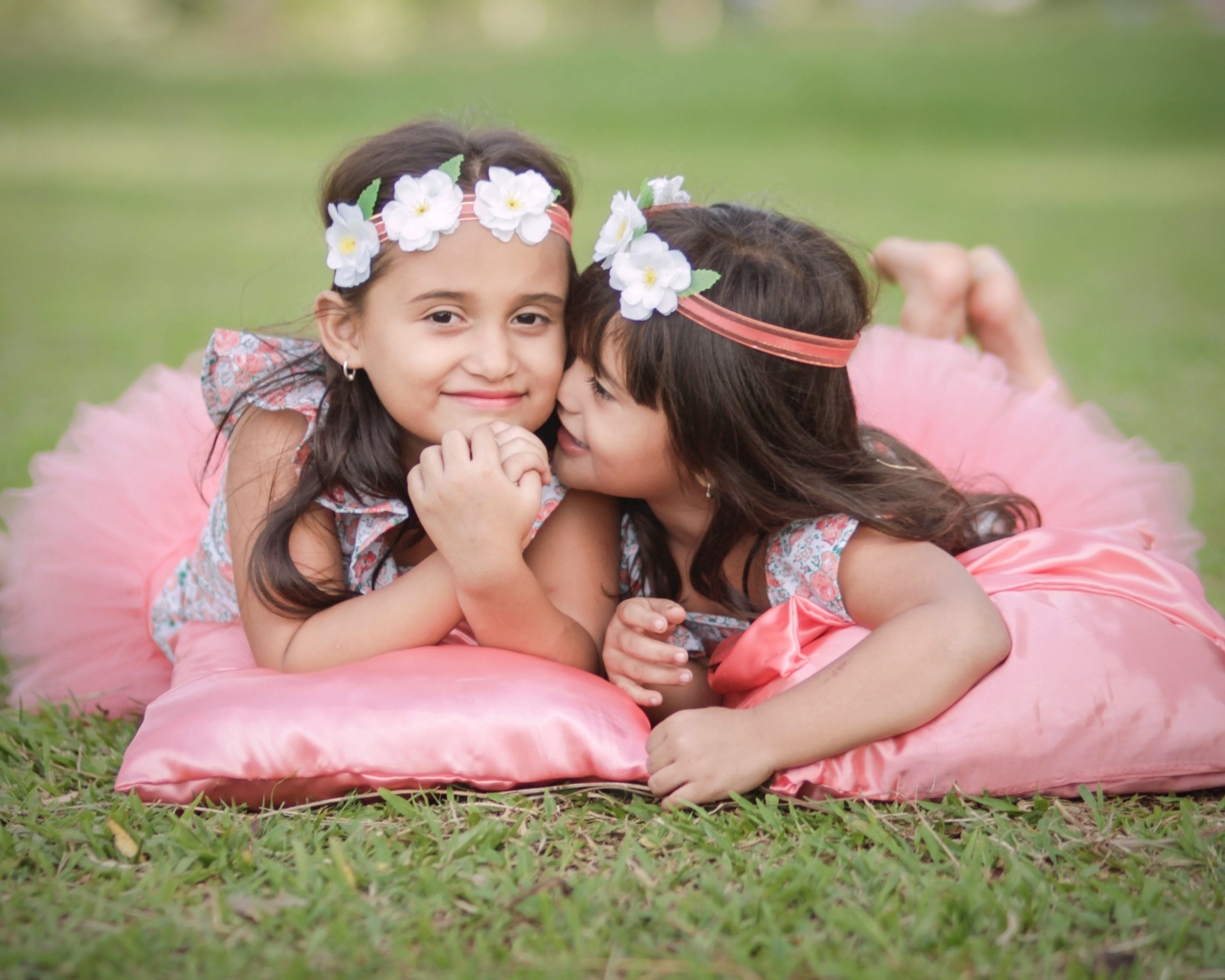 Две маленькие девочки лежат на подушках на траве