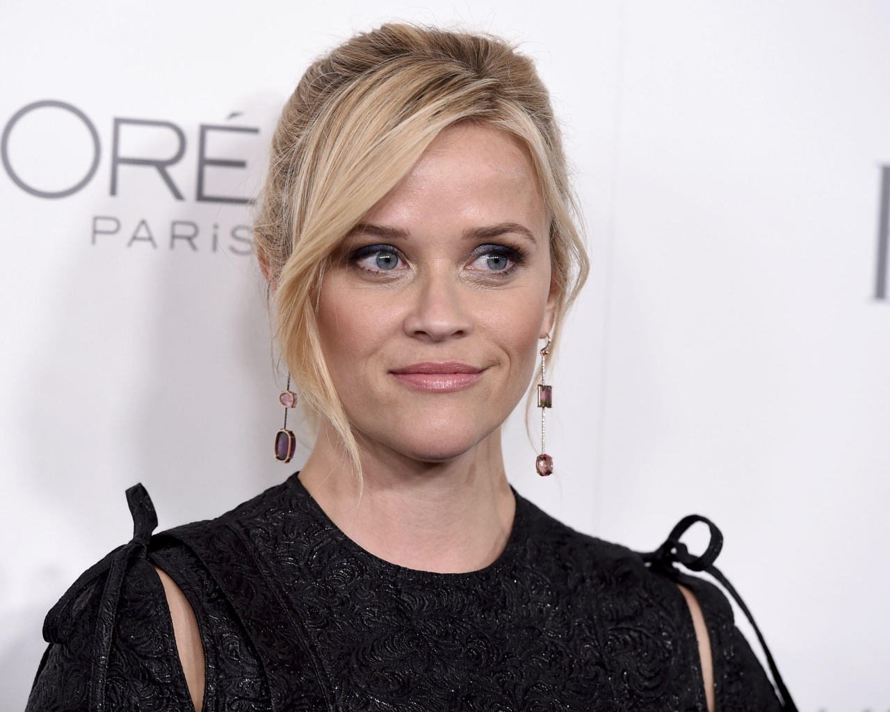 Actress Reese Witherspoon in a black dress against a wall