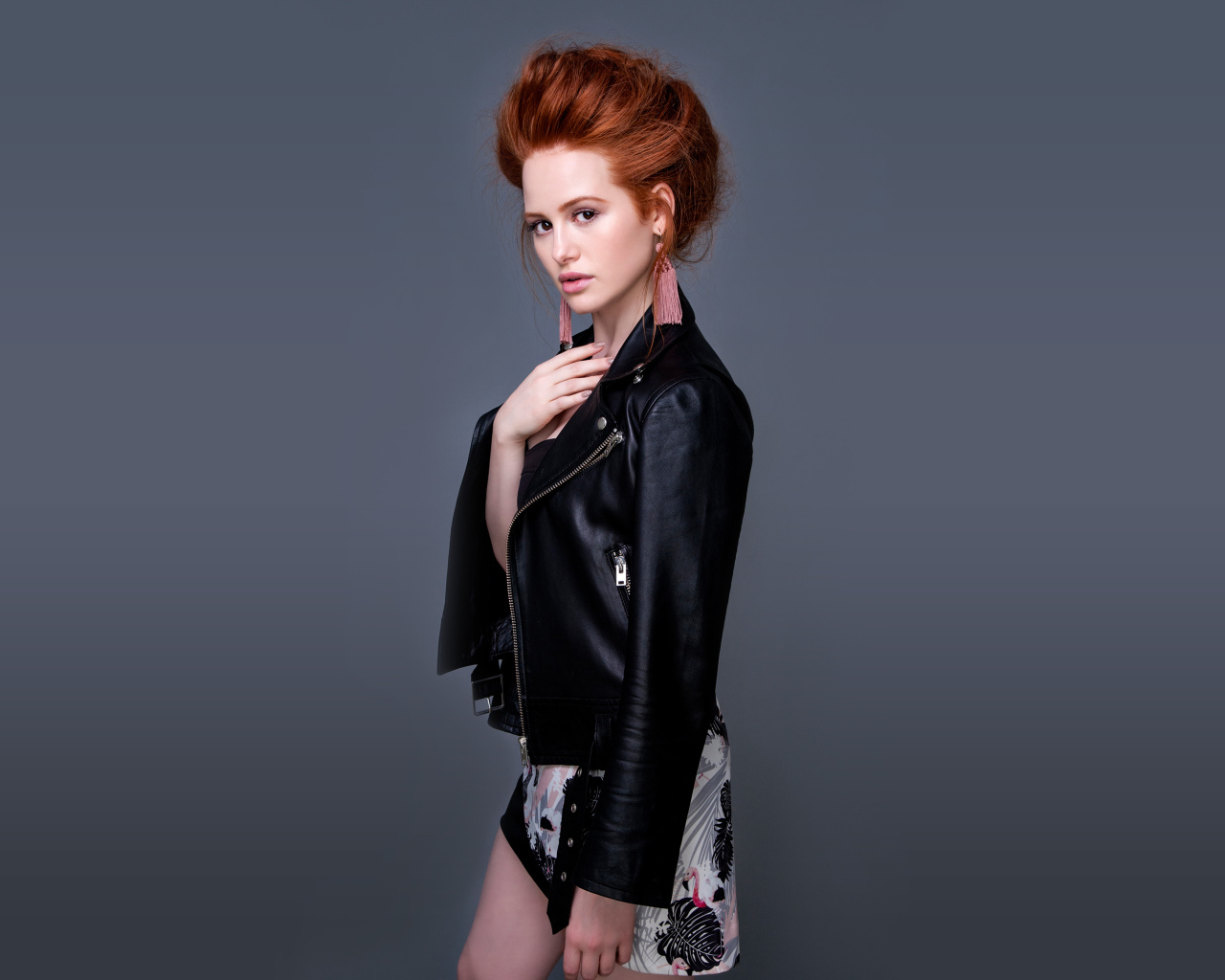 Рыжеволосая актриса Мэделин Петш в черной куртке на сером фоне