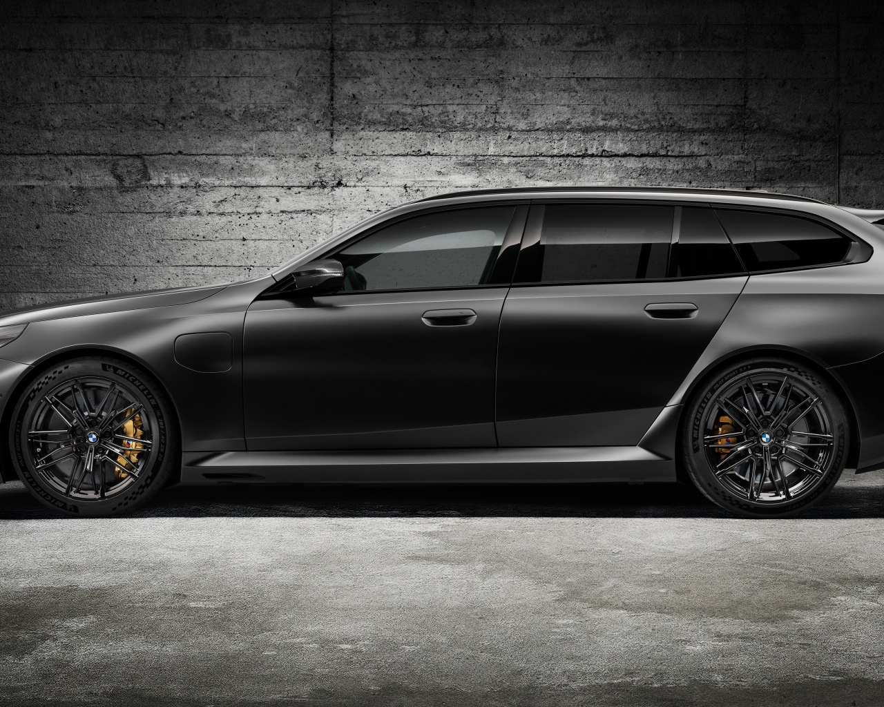 Вид сбоку на черный автомобиль BMW M5 Touring 2024 года