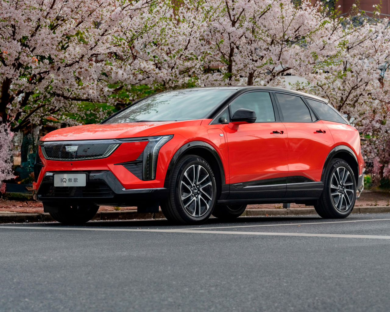 Красный Cadillac Optiq Sport 2024 года у цветущих деревьев