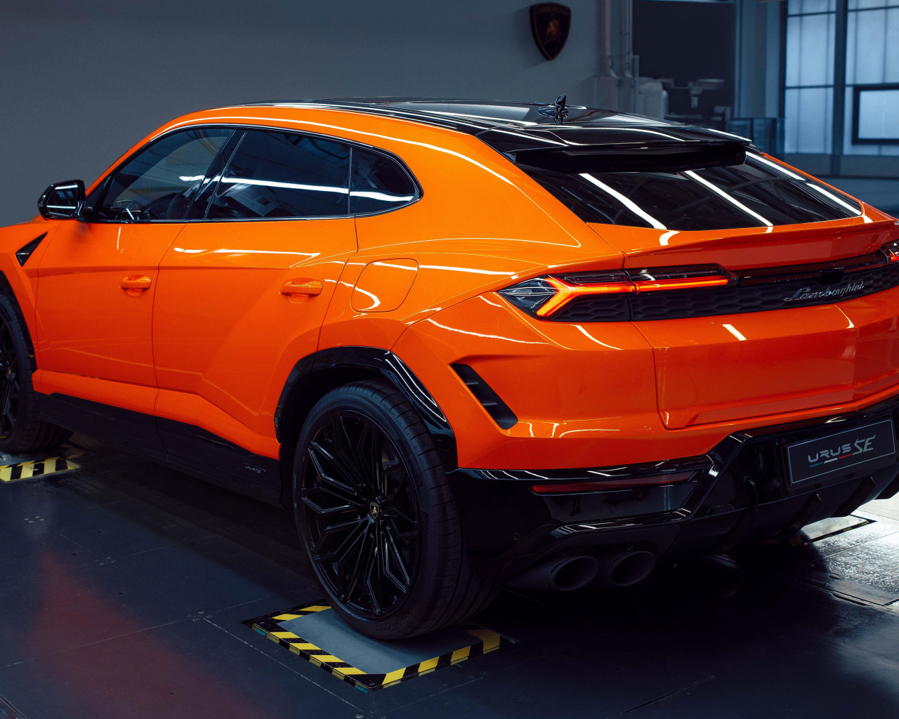 Вид сзади на оранжевый автомобиль  Lamborghini Urus SE Plug-In Hybrid 2024 года