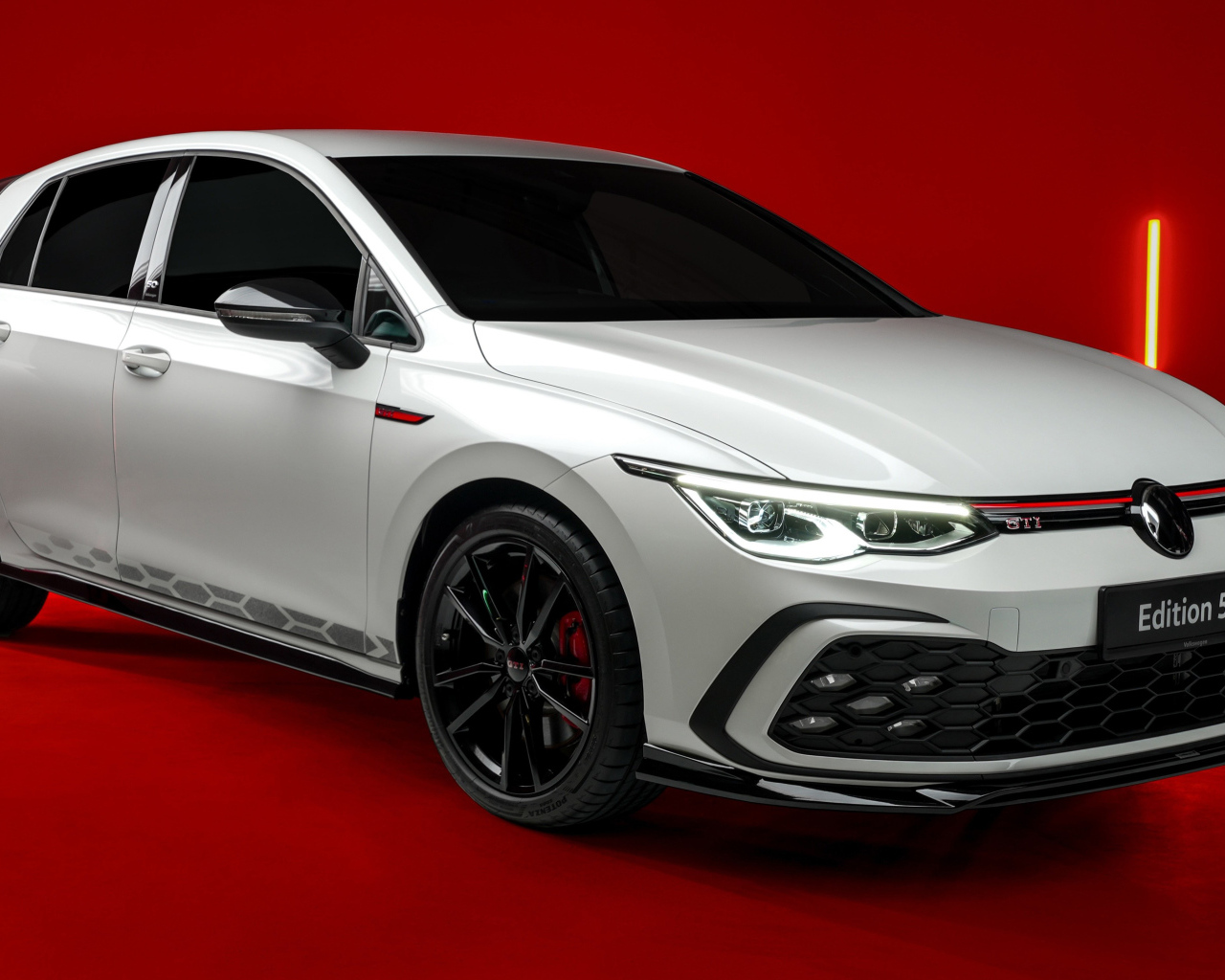 Автомобиль Volkswagen Golf GTI Edition 50 2024 года на красном фоне