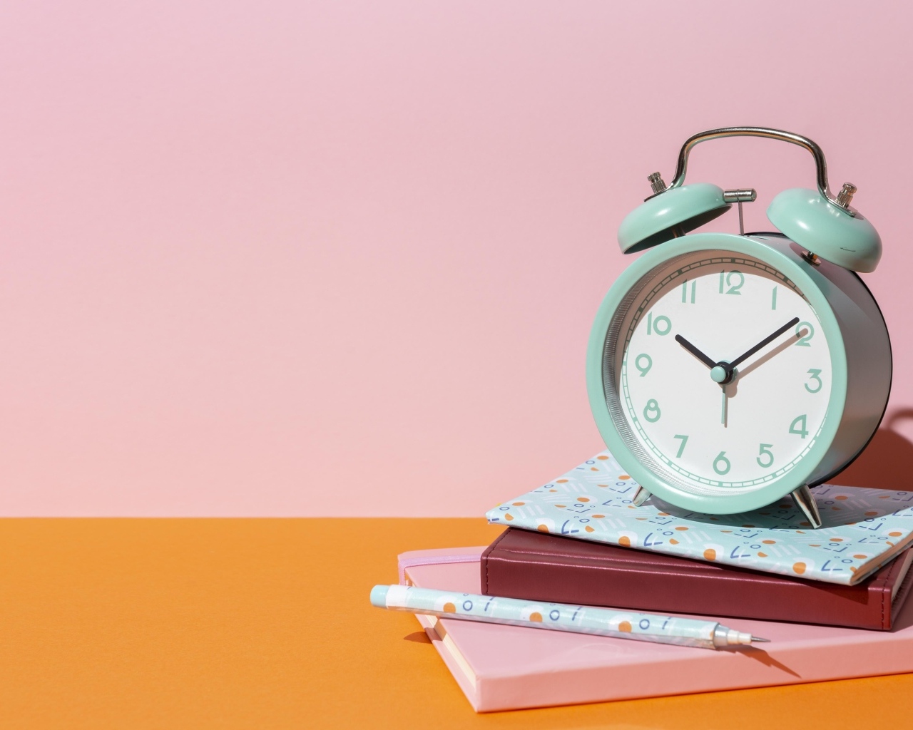 Будильник с книгами на розовом фоне