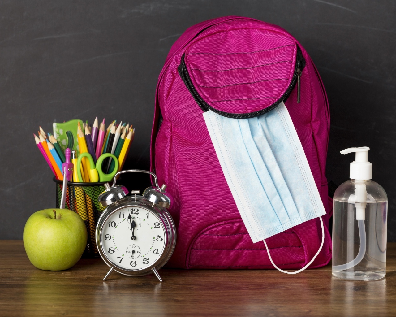 Рюкзак на столе с будильником, ручками и яблоком