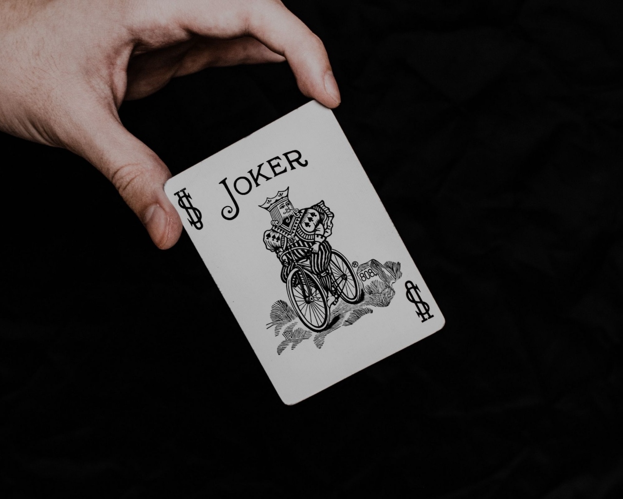 Карта Джокер в руке на черном фоне