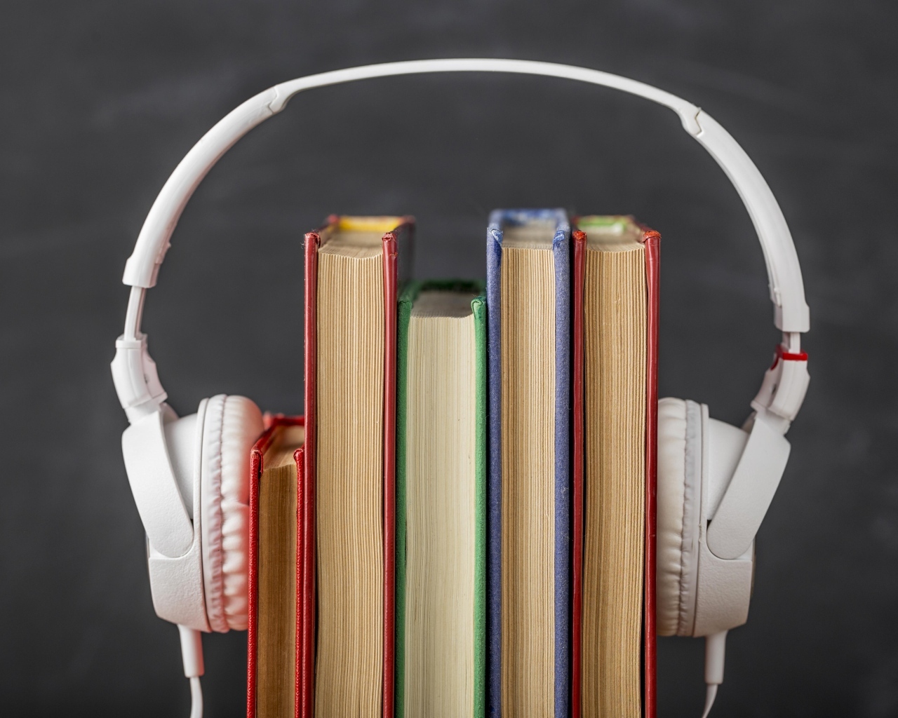 Разноцветные книги с белыми наушниками на сером фоне