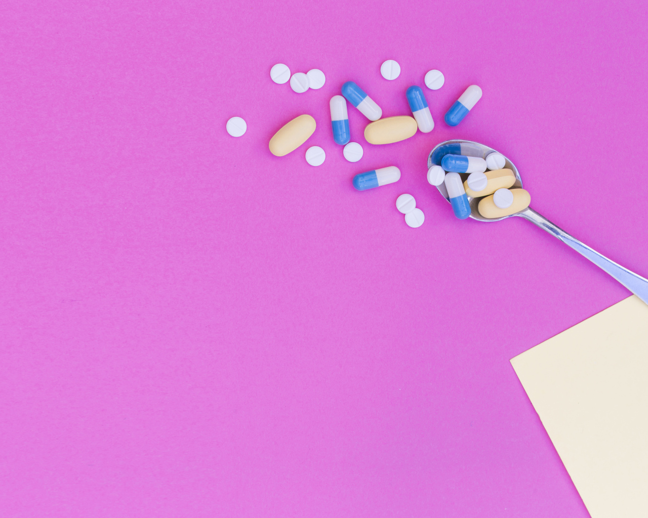 Таблетки с ложкой на розовом фоне