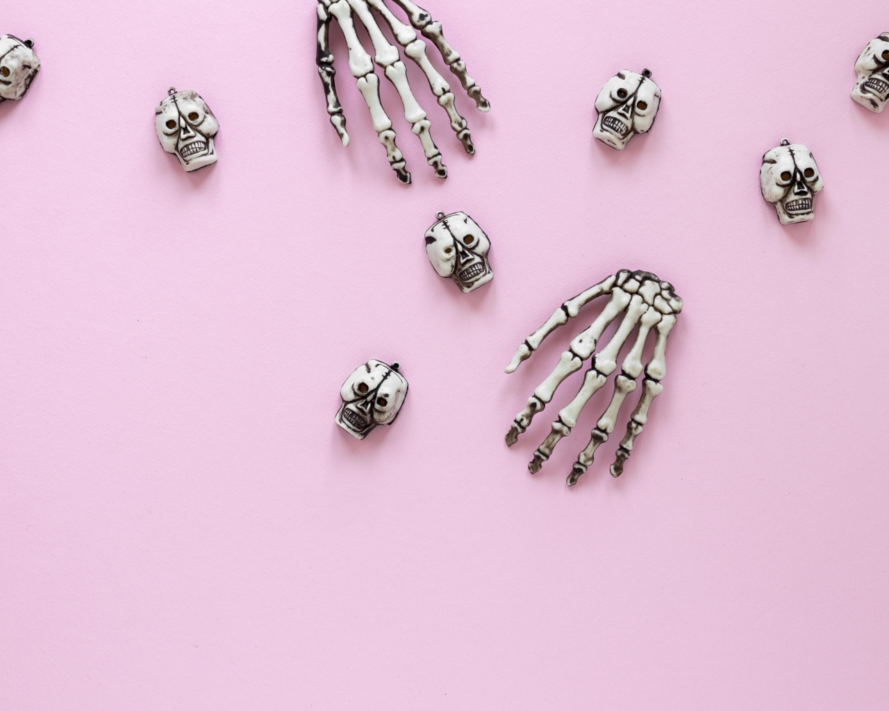 Кисти рук скелета и черепа на розовом фоне