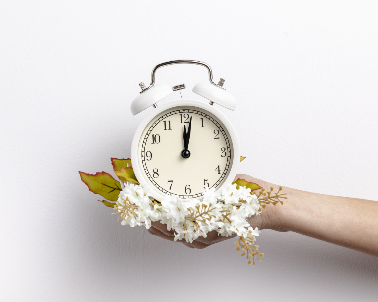 Белый будильник в руке с цветами на сером фоне