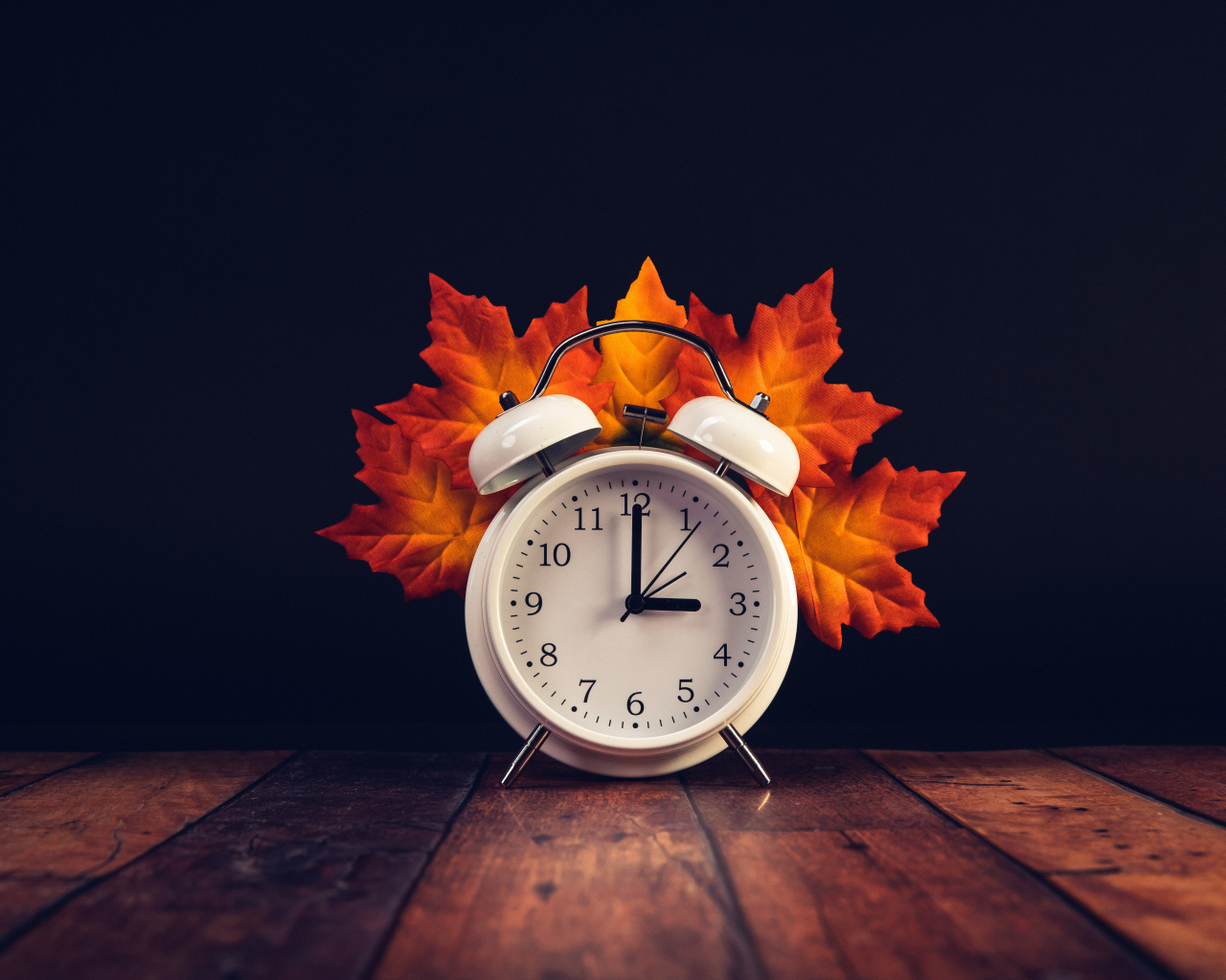 Белый будильник с оранжевыми листьями на столе