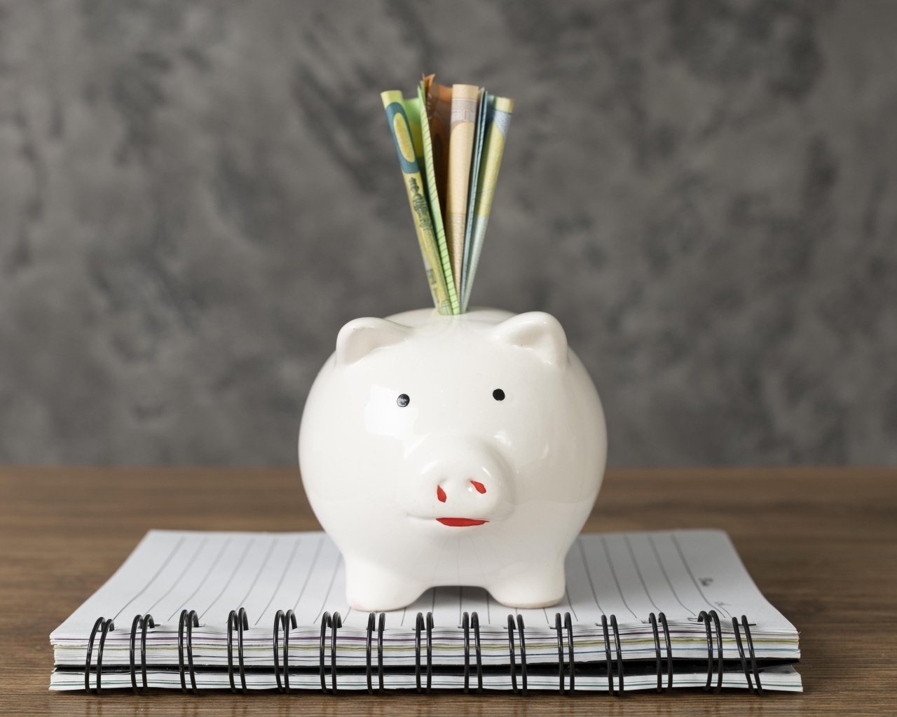 Свинья копилка с купюрами на столе с блокнотом