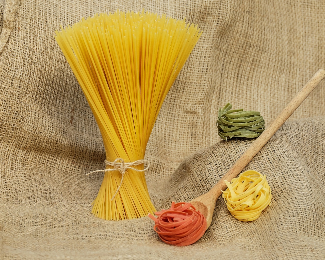 Разноцветные макаронные изделия с деревянной ложкой на мешке