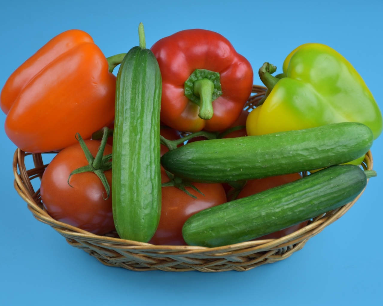 Перец, помидоры и огурцы в корзине на голубом фоне