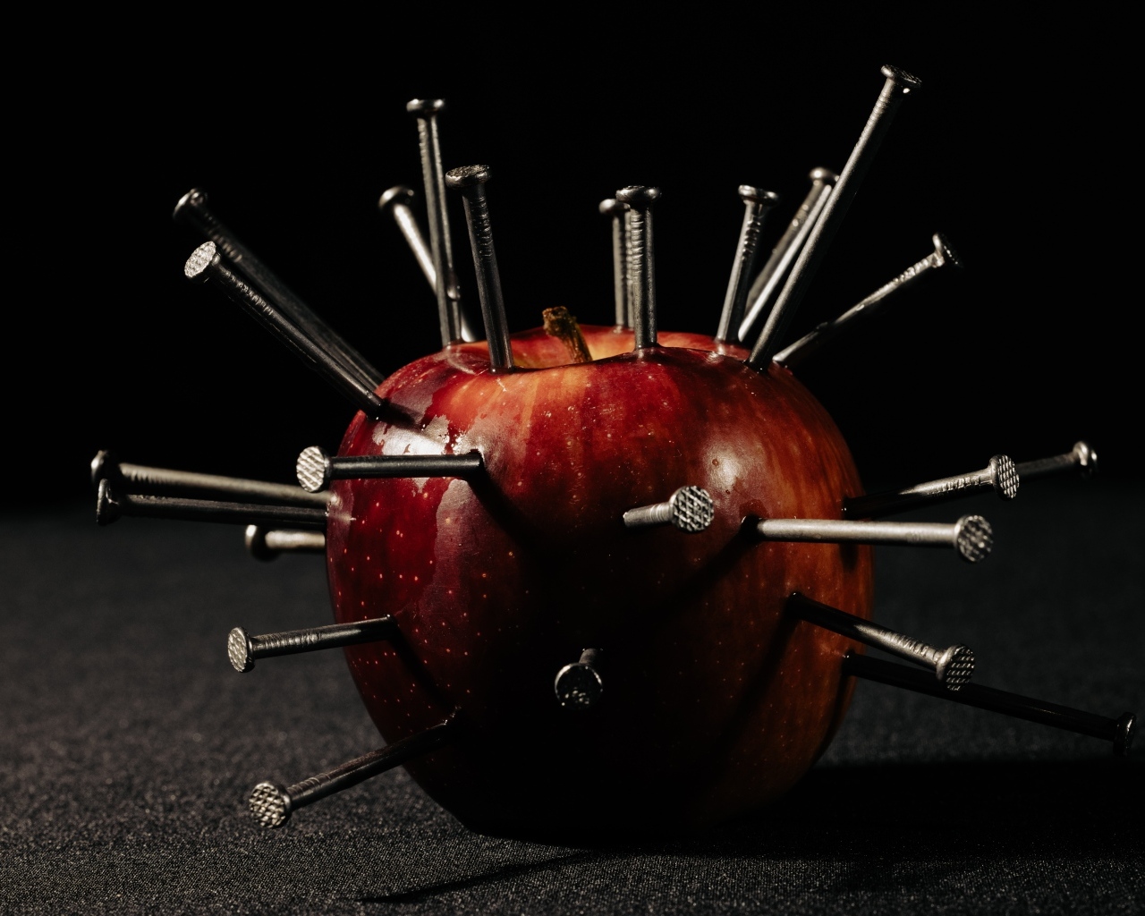 Красное яблоко утыканное гвоздями на темном фоне