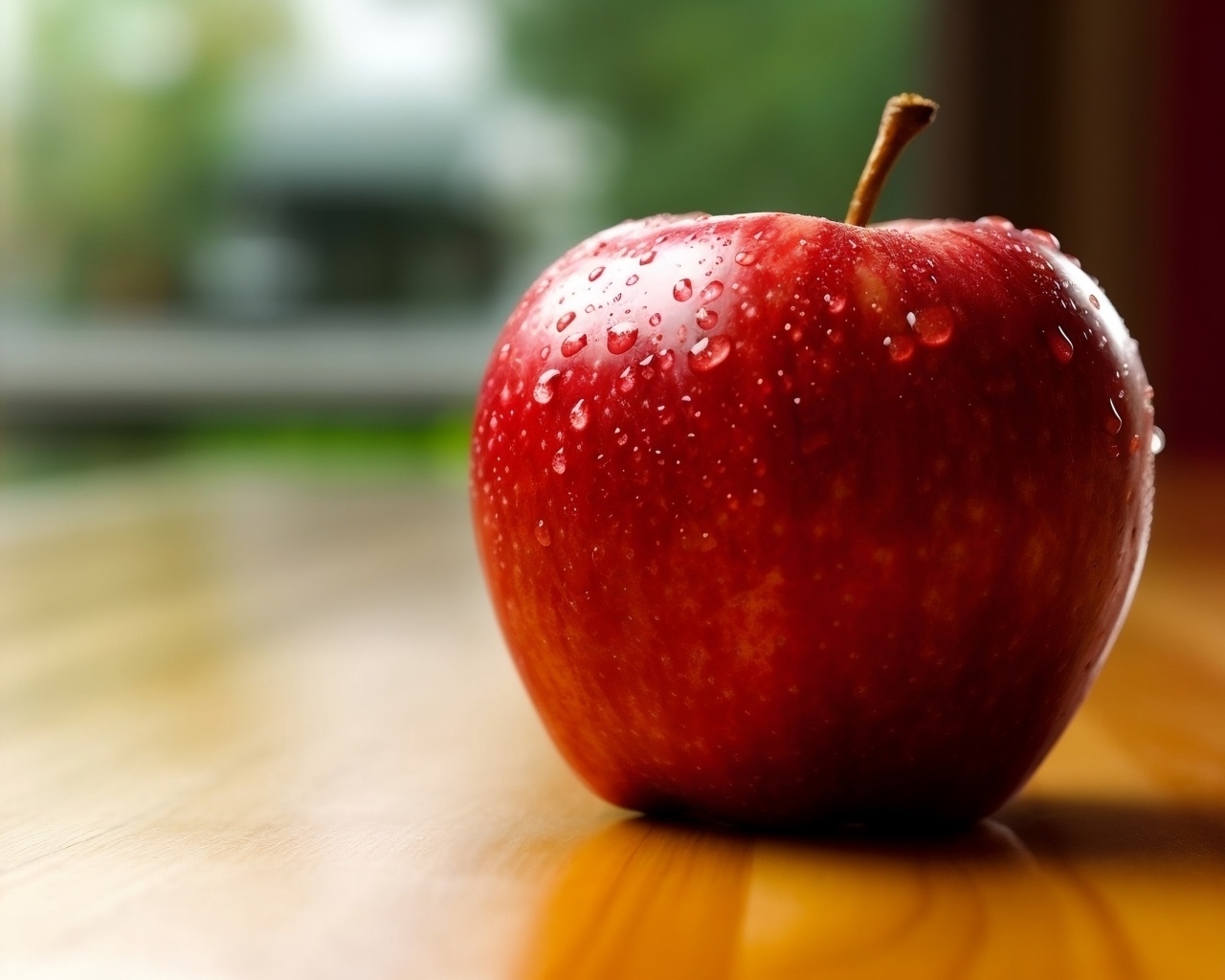 Красное яблоко в каплях воды на столе