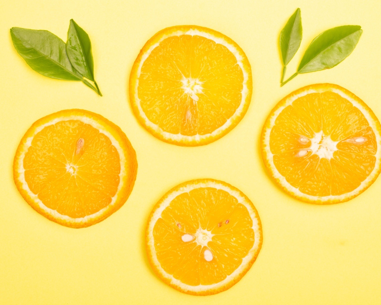 Нарезанный апельсин с зелеными листьями на желтом фоне