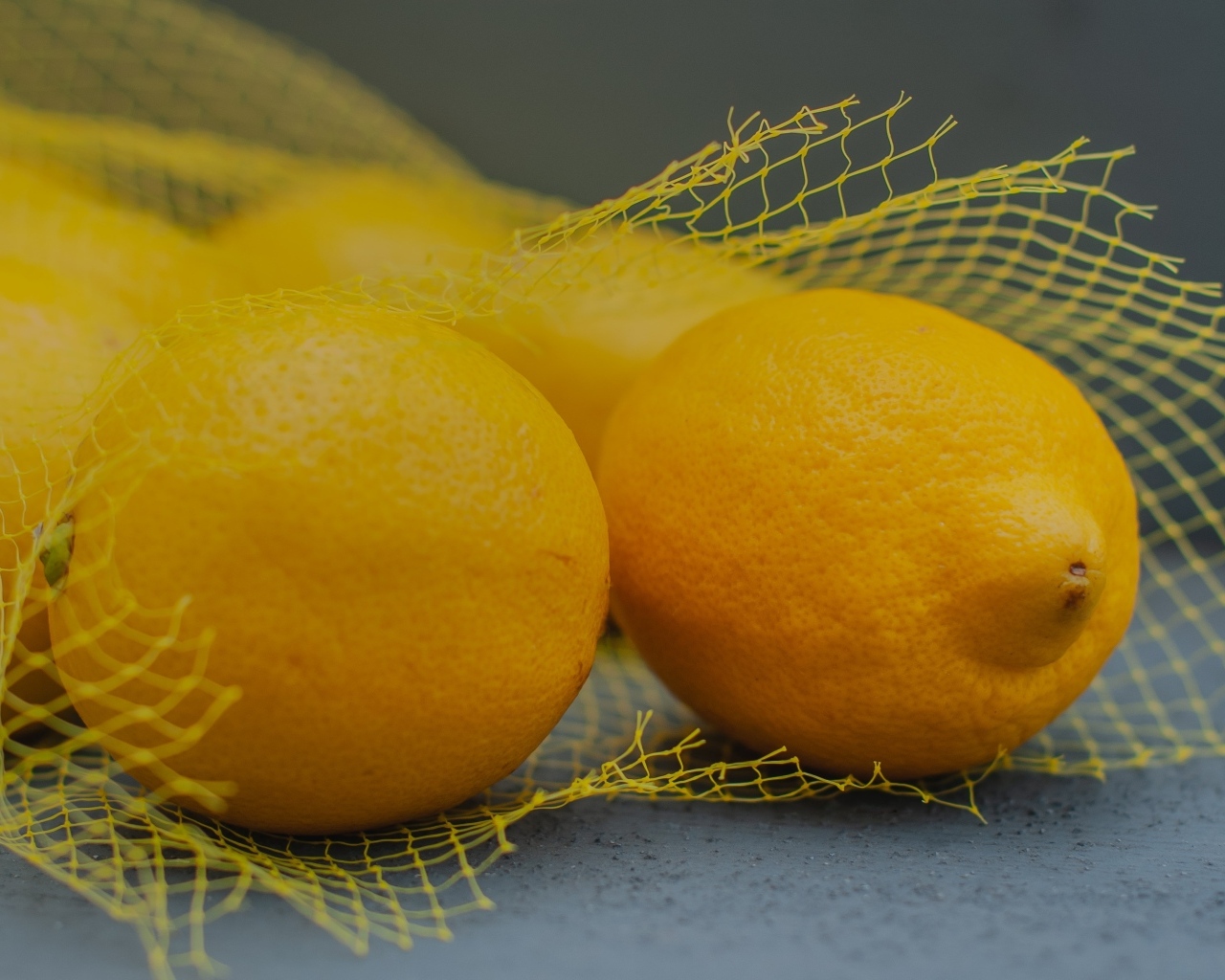 Желтые лимоны в сетке на сером столе