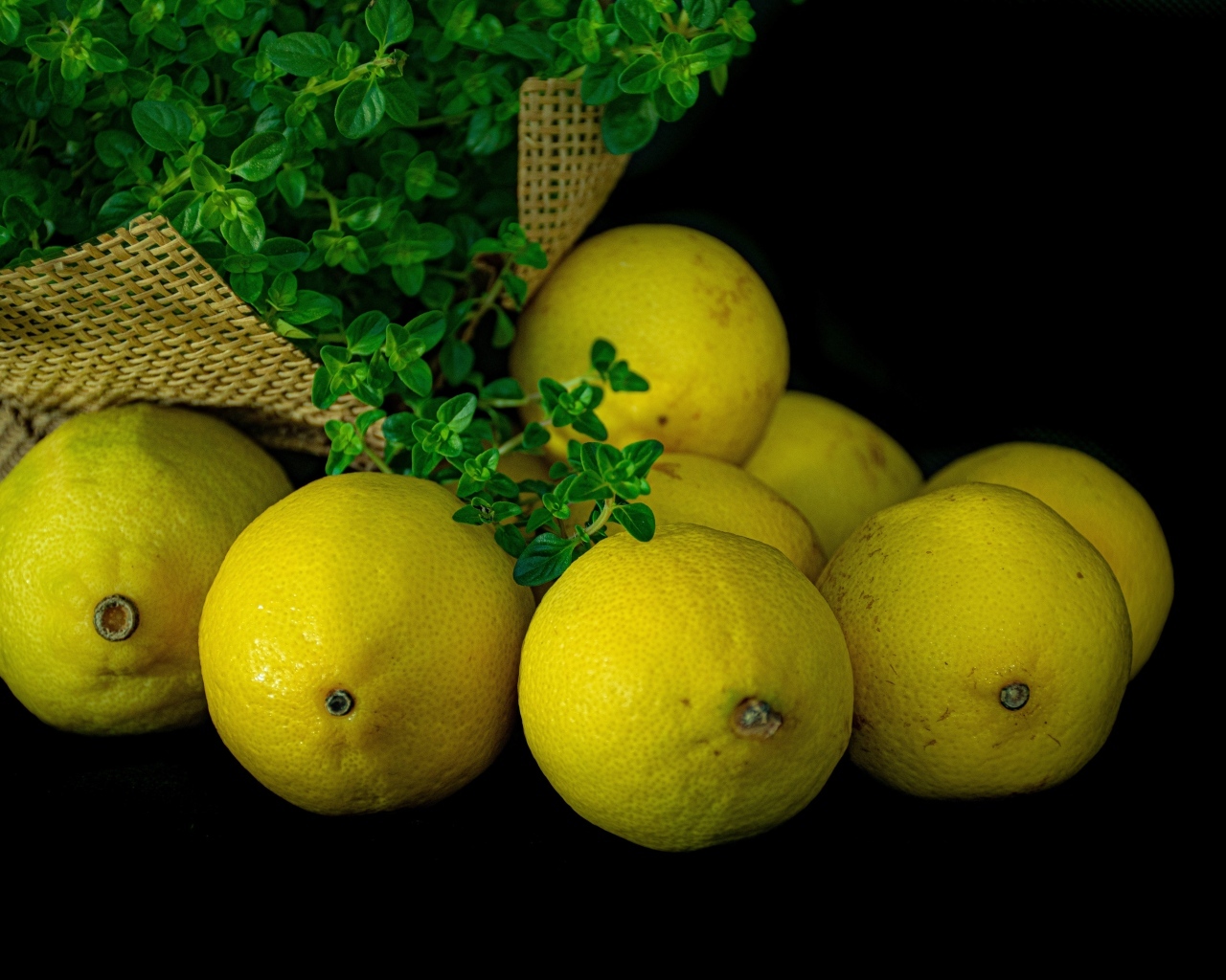 Желтые лимоны на черном столе с зеленью