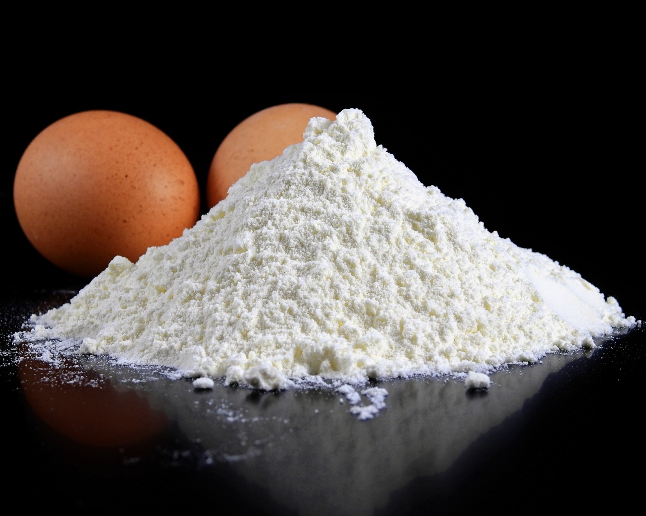 Мука на черном столе с куриными яйцами