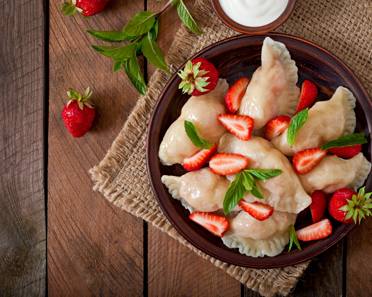 Вареники с клубникой на столе со сметаной