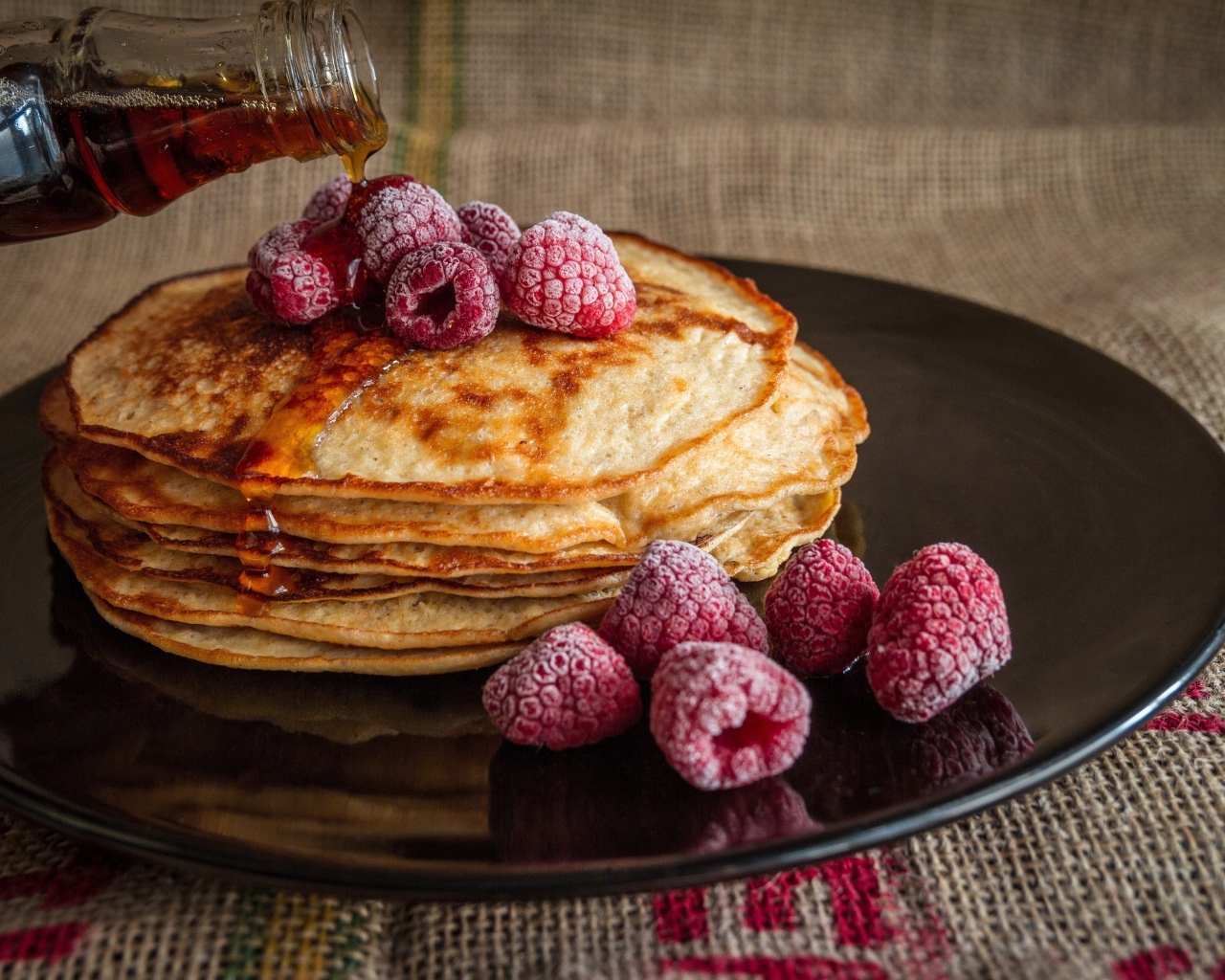 Тонкие блинчики на черной тарелке с ягодами малины и медом