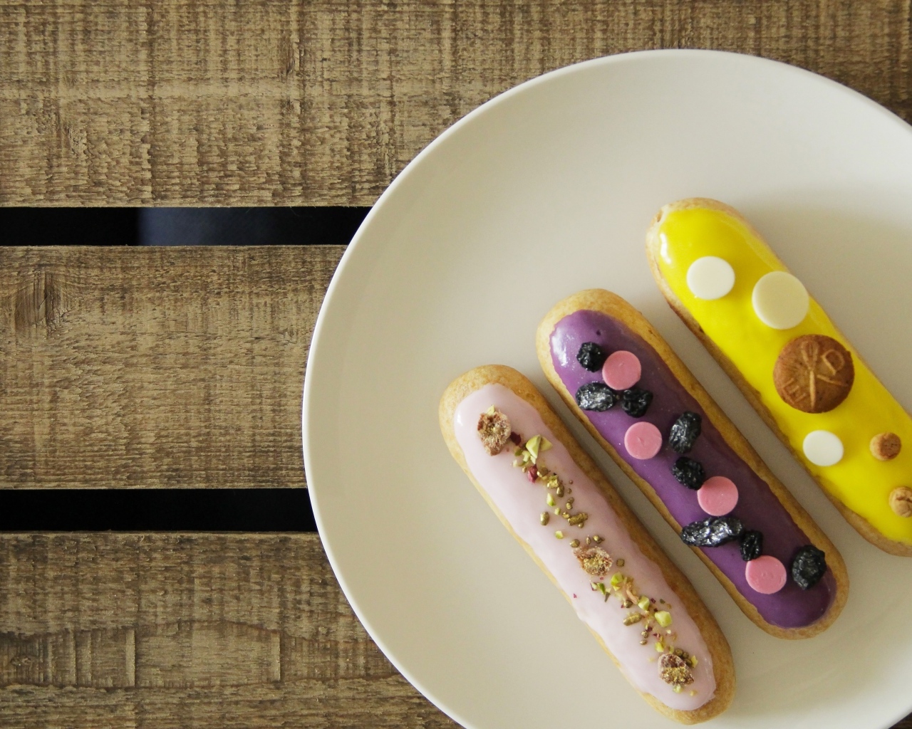 Три эклера на белой тарелке на деревянном столе