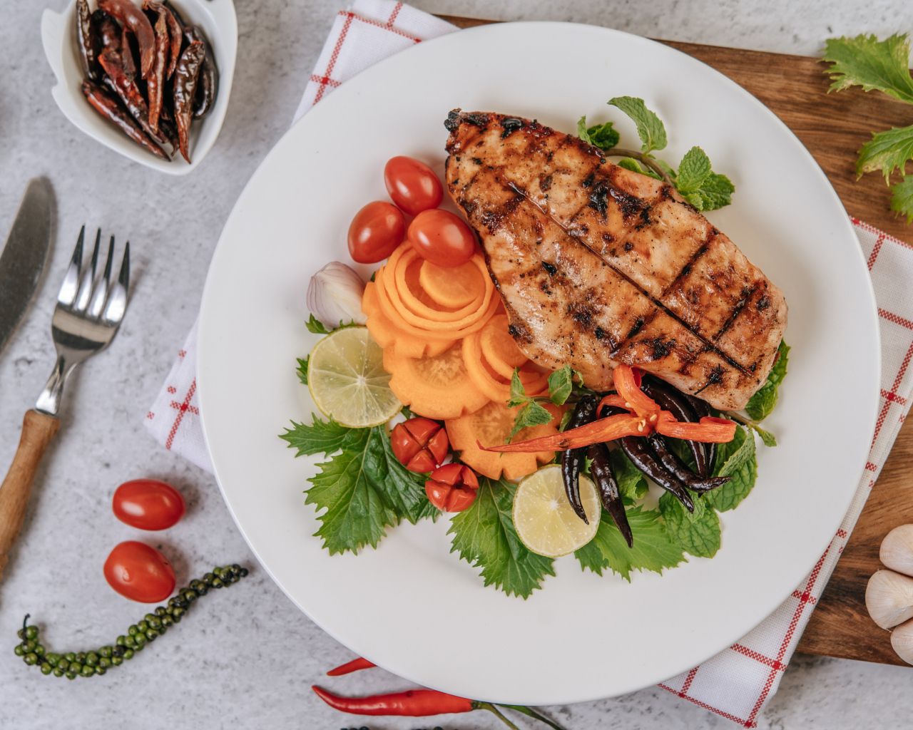 Кусок жареной курицы на большой белой тарелке с овощами