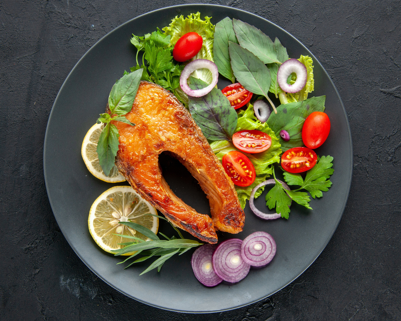 Жареная рыба на тарелке с зеленью,  лимоном и помидорами