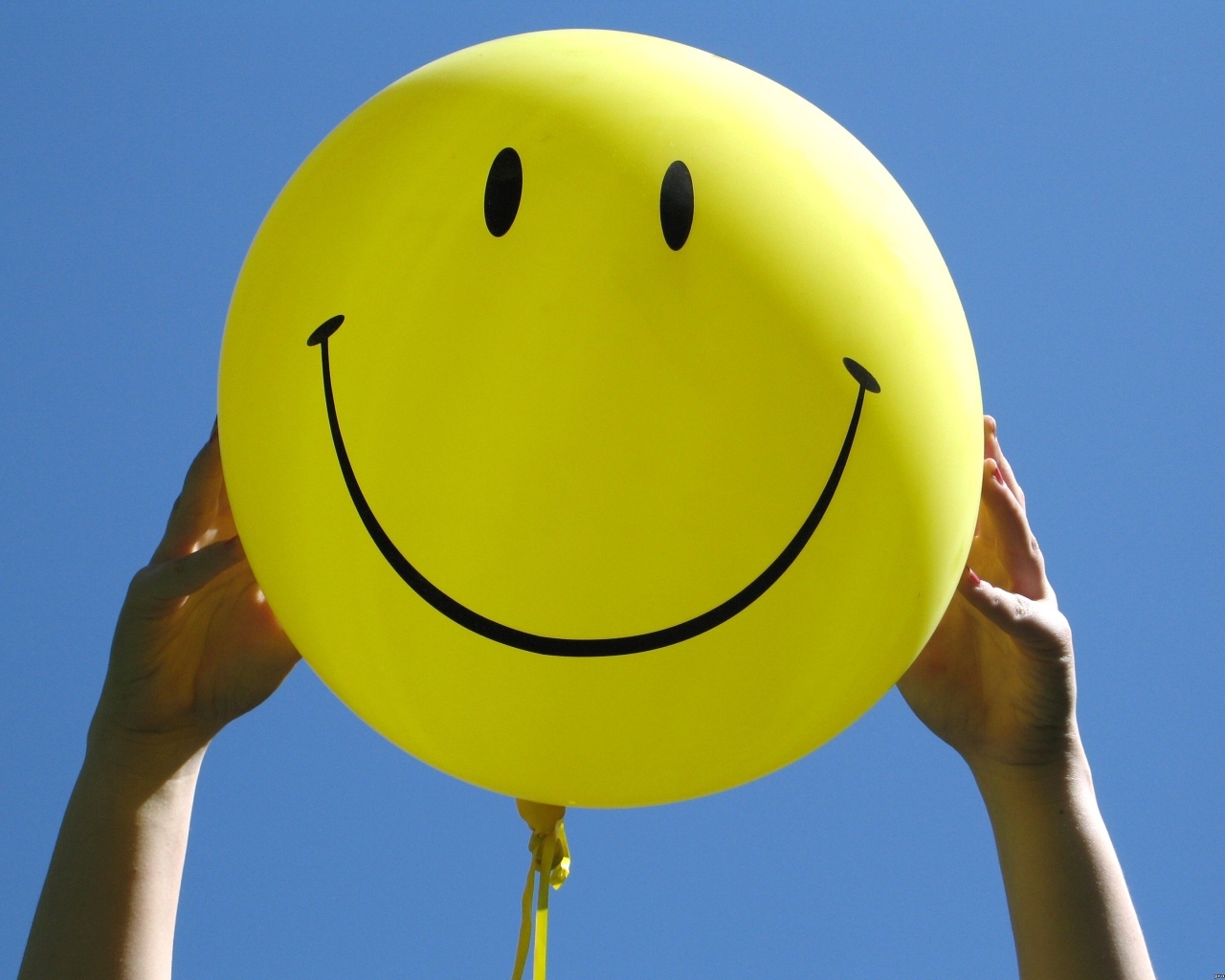 Желтый шарик с улыбкой в руках на голубом фоне