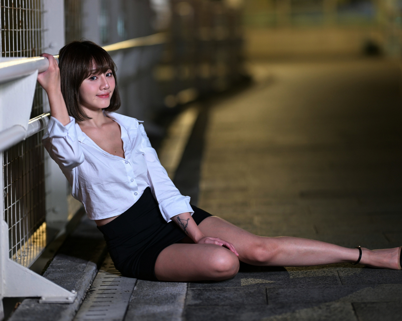 Девушка в черной юбке и белой рубашке сидит на дороге