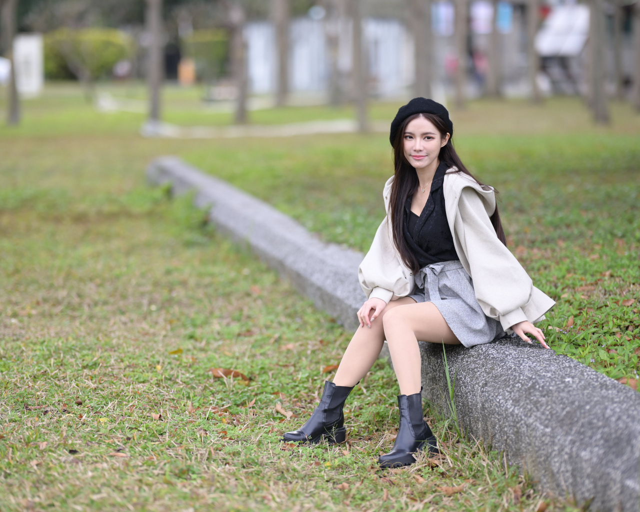 Девушка в пальто сидит на земле в парке