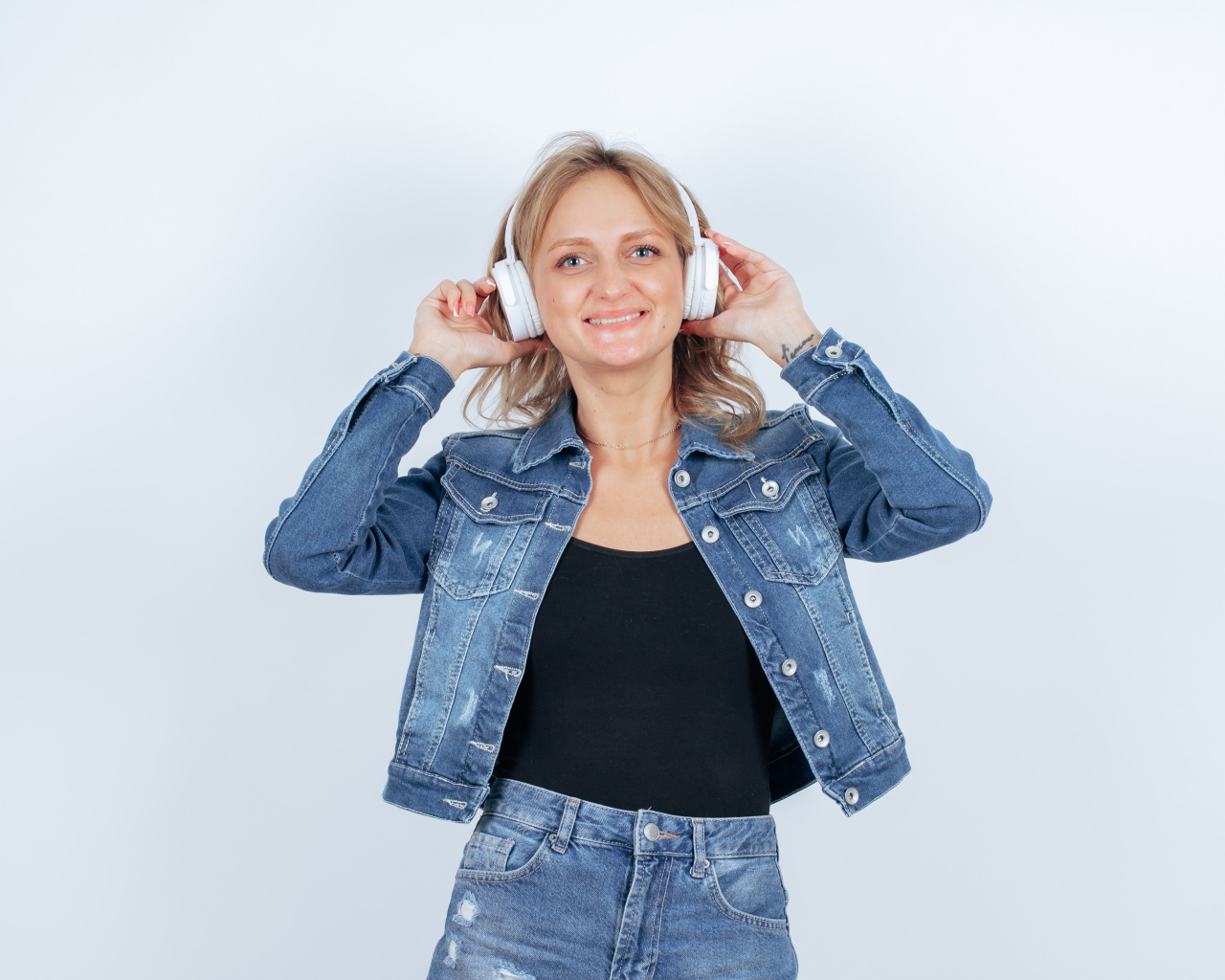 Девушка в джинсовом костюме с наушниками на голове на фоне стены