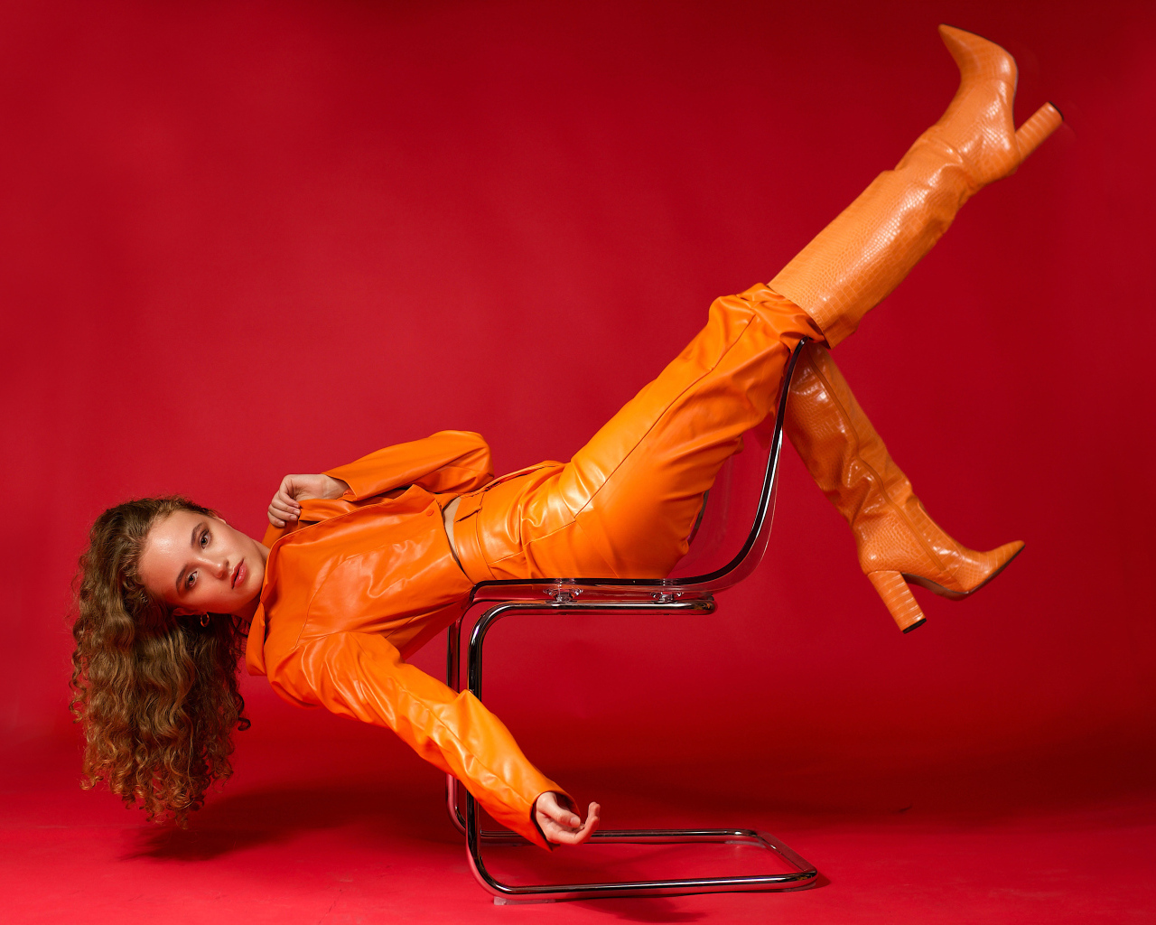 Девушка в кожаном костюме лежит на кресле на красном фоне