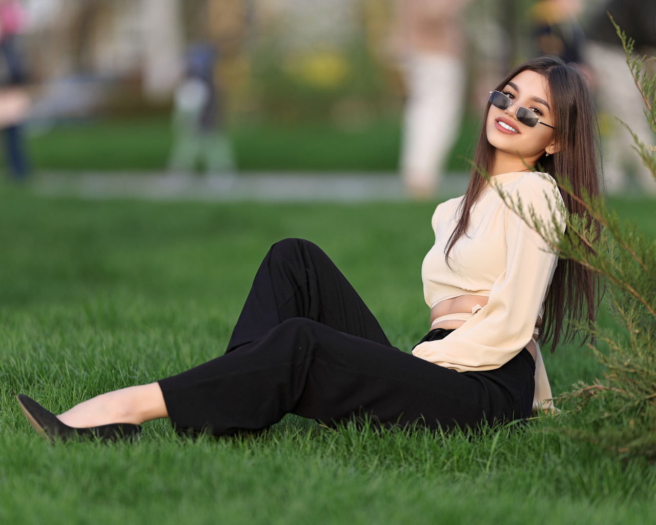 Девушка в черных брюках и блузке сидит на траве