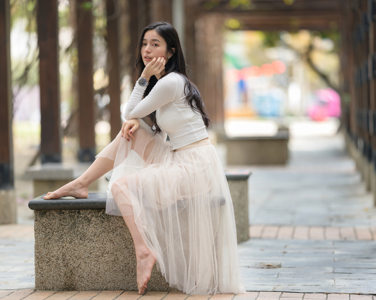 Девушка азиатка в белой юбке из фатина сидит на лавке