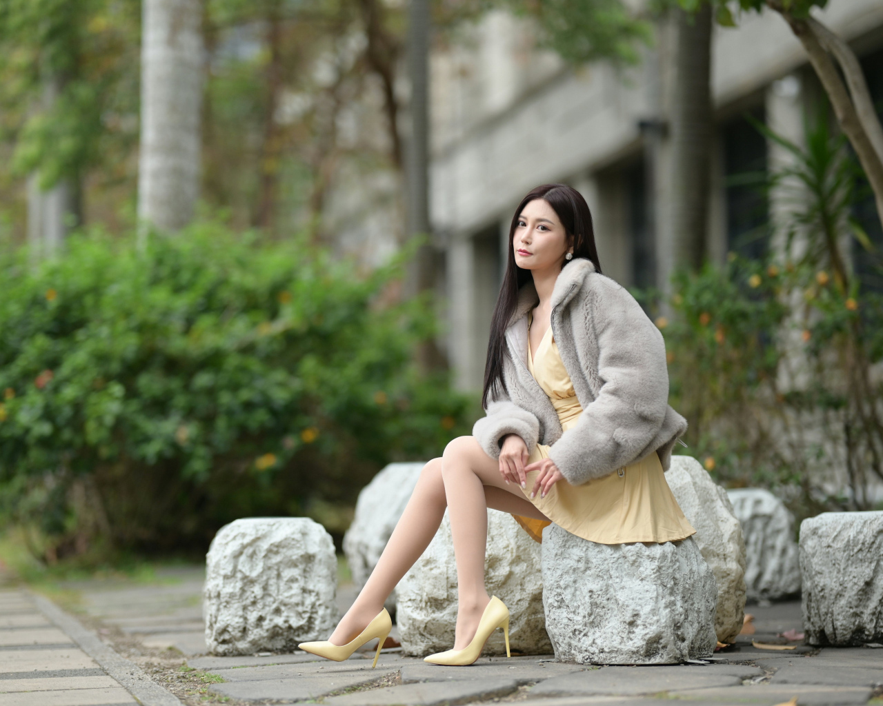 Азиатка в шубе сидит на квадратном камне