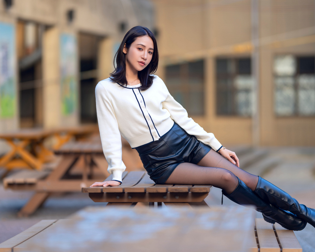 Азиатка в черных кожаных сапогах лежит на деревянном столе