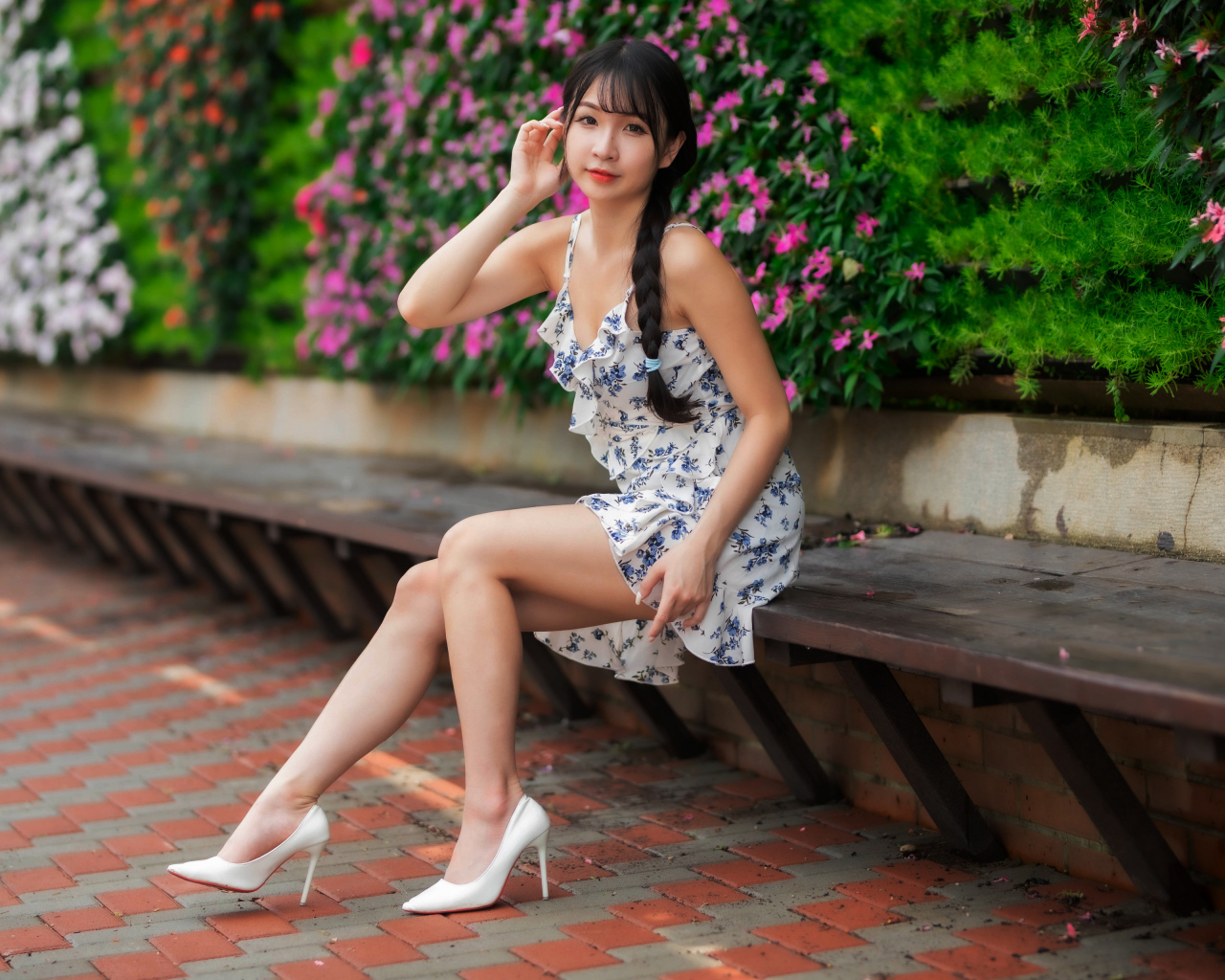 Азиатка в платье сидит на лавке у цветущих растений