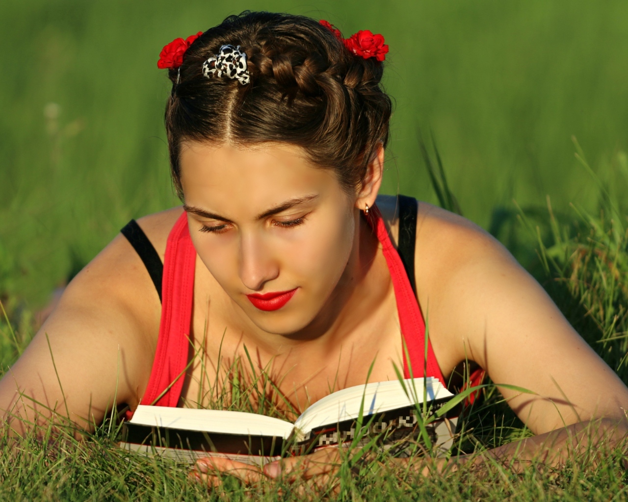 Красивая девушка читает книгу лежа на траве