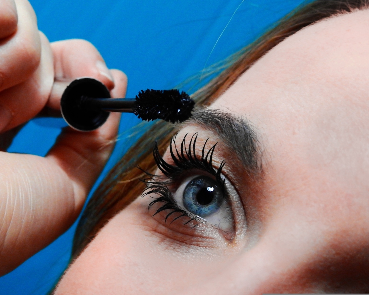 Голубоглазая девушка красит ресницы тушью