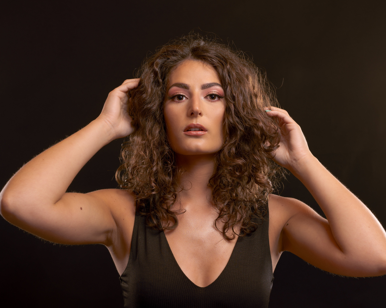 Кудрявая девушка держит руки в волосах на черном фоне