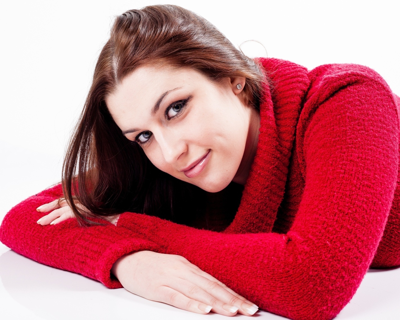 Милая брюнетка в красном свитере лежит на белом фоне
