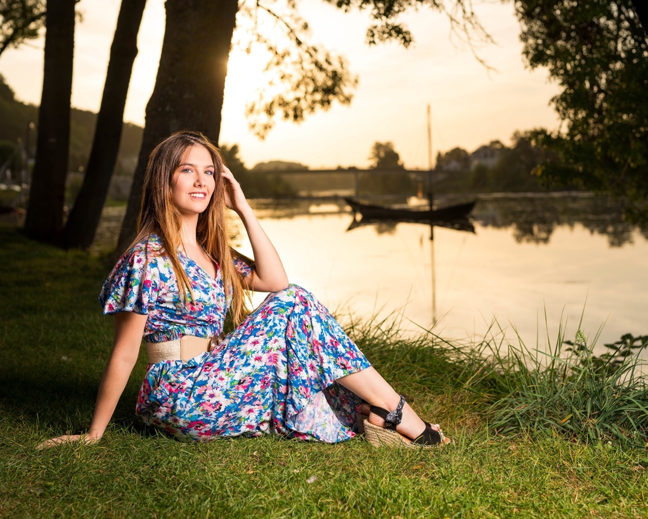 Милая девушка в платье сидит на берегу реки в парке