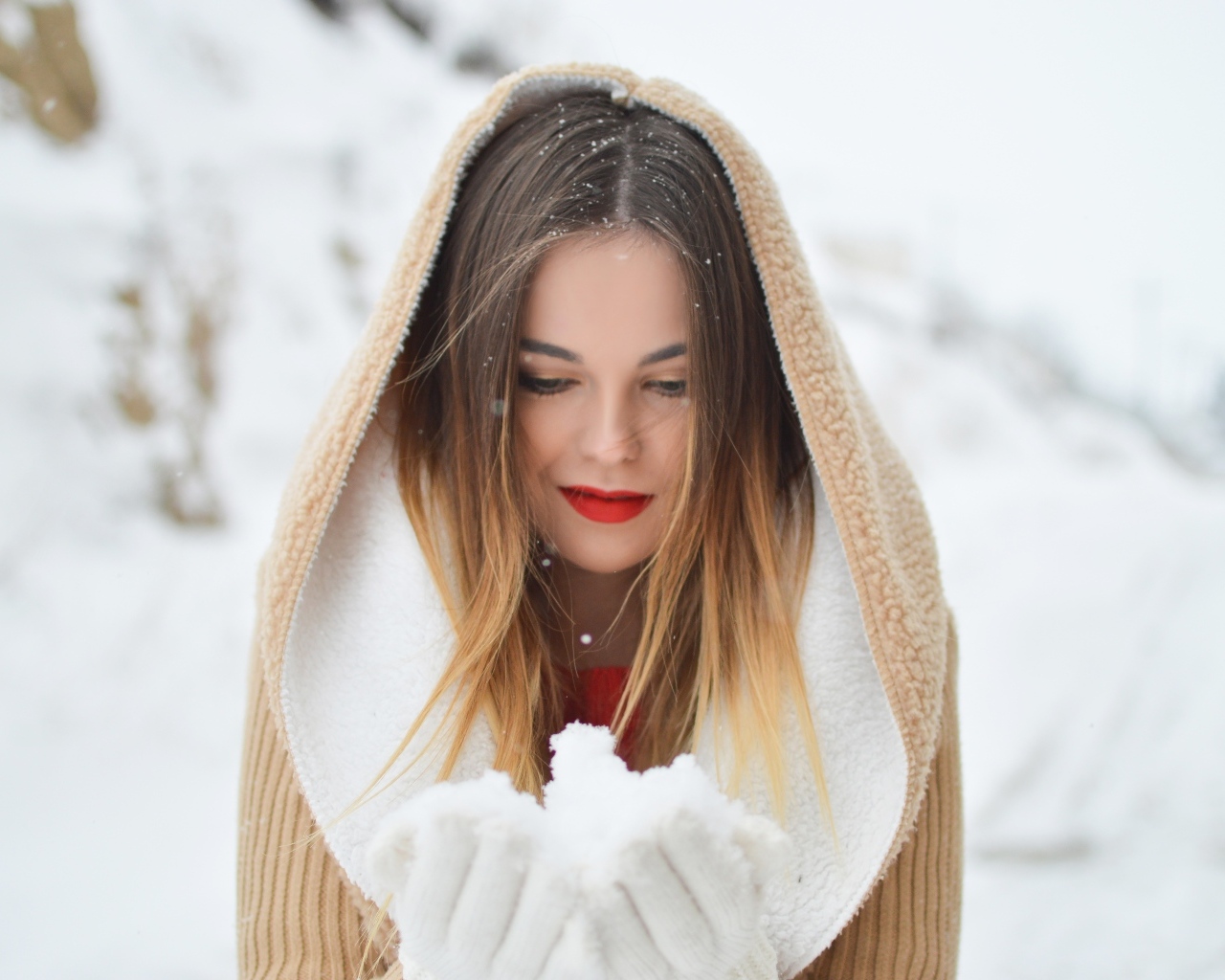 Милая девушка в капюшоне держит снег в ладонях